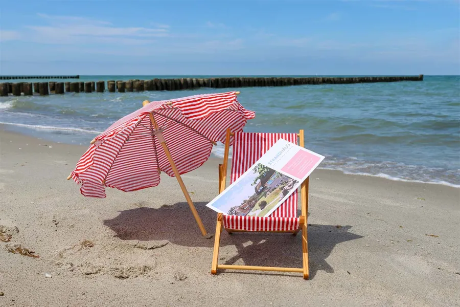 Ein Gutschein des STRANDHAUS Ahrenshoop liegt in einem Miniaturstrandstuhl am sonnigen Strand auf dem Fischland-Darß.