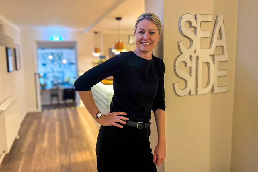 Lächelnde Mitarbeiterin steht neben einem SEASIDE Schriftzug an der Wand im Boutique-Hotel STRANDHAUS Ahrenshoop