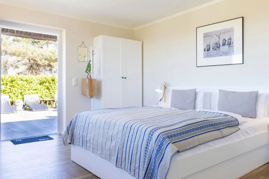 Terrassenzimmer im STRANDHAUS Ahrenshoop mit weißem Doppelbett, Nachttischlampen und direktem Terrassenzugang.