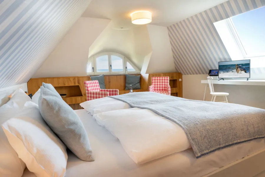 Suite im STRANDHAUS Ahrenshoop mit Dachschraege, blau-weiss gestreifter Tapete und Blick auf die Ostsee.