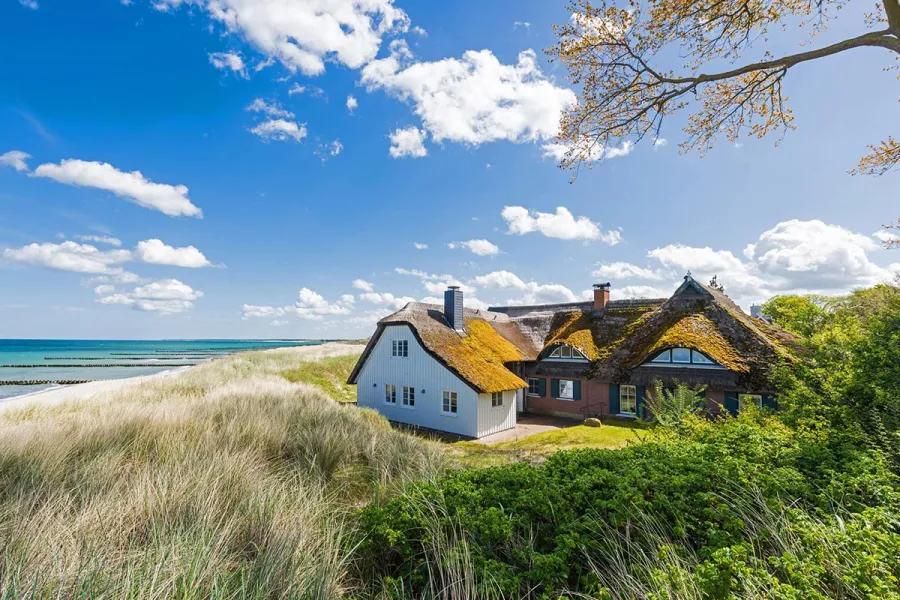 Typische Reetdachhäuser auf dem Fischland-Darß mit Blick auf Dünen, Strand und Ostsee im Frühling.