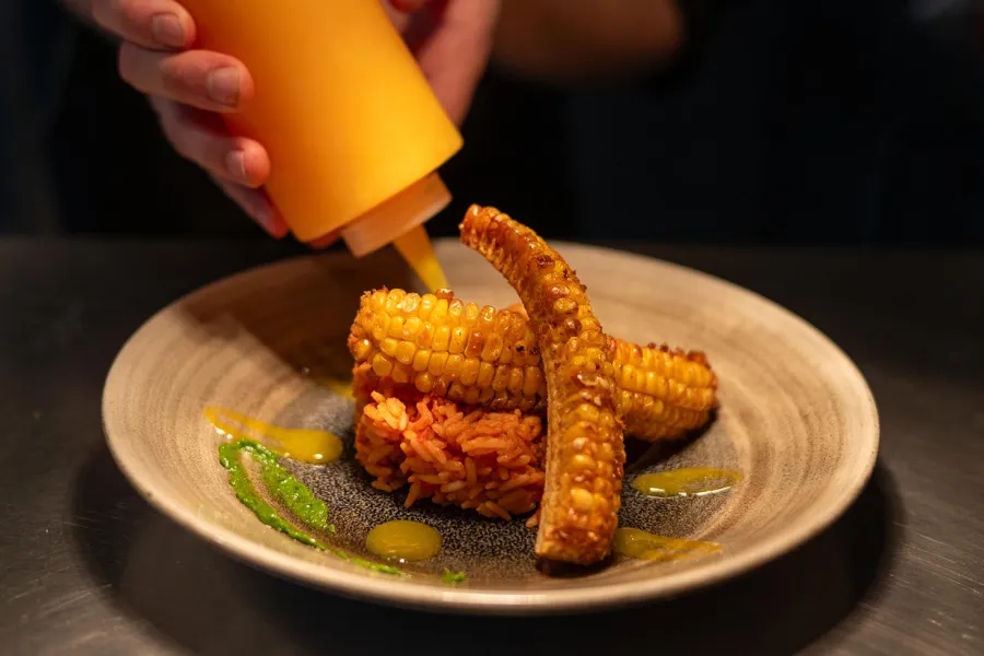 Ein Teller mit Resi und Mais wird am Pass einer Restaurantküche dekoriert.