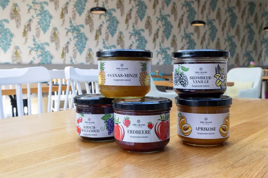 Fünf Gläser hausgemachte Marmelade von THE GRAND Ahrenshoop in verschiedenen Sorten auf einem Holztisch im STRANDHAUS.