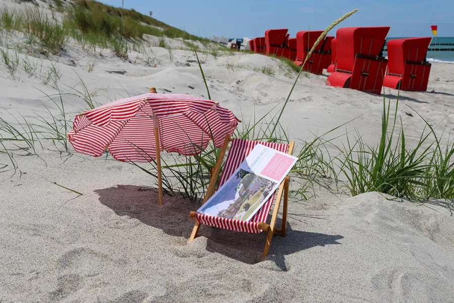 Miniatur-Liegestuhl mit STRANDHAUS-Gutschein im Sand vor roten Strandkoerben an der Ostsee auf dem Fischland-Darß.