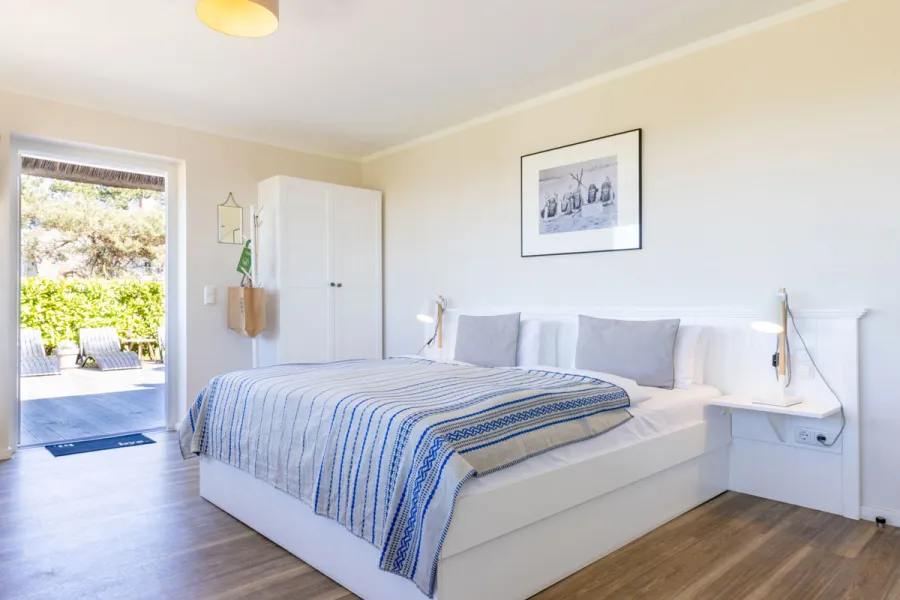 Helles Doppelzimmer im STRANDHAUS Ahrenshoop mit blau-weisser Bettwaesche und offenem Terrassenausgang ins Gruene.