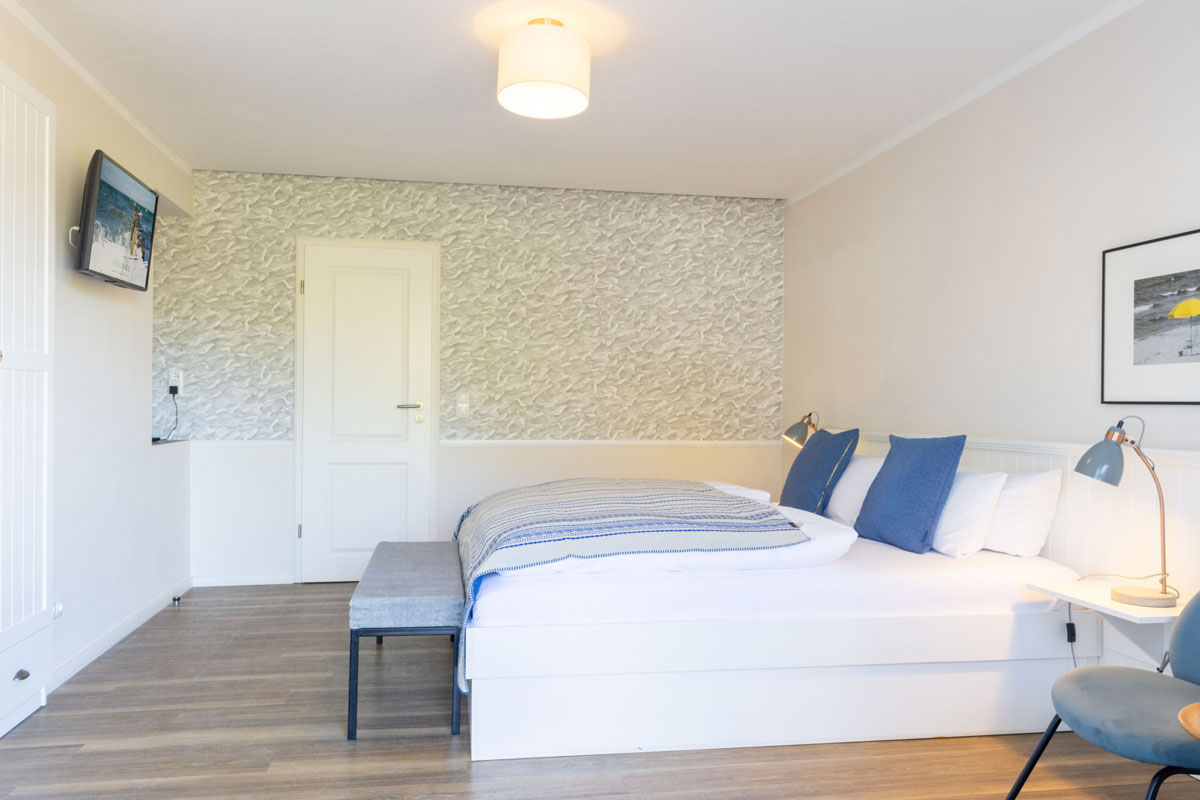 Doppelzimmer Petit im STRANDHAUS Ahrenshoop mit Doppelbett, blauer Tagesdecke und strukturierter Akzentwand.