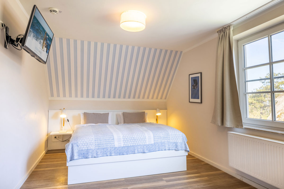 Doppelzimmer im STRANDHAUS Ahrenshoop mit Doppelbett, gestreifter Tapete und Blick ins Grüne.