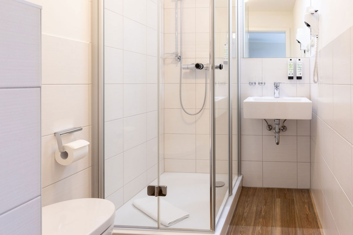 Bad im Einzelzimmer des STRANDHAUS Ahrenshoop mit Glasdusche, WC, Waschbecken und Spiegel.