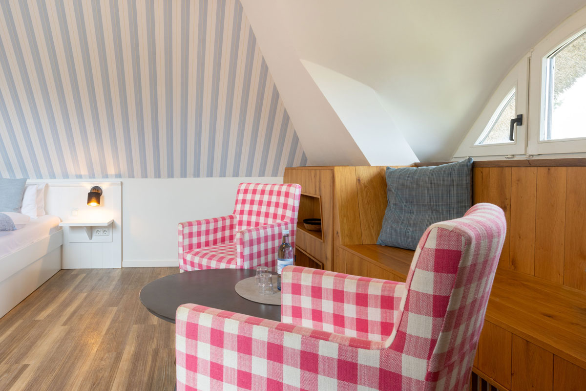 Sitzecke in der Familiensuite des STRANDHAUS Ahrenshoop mit zwei karierten Sesseln, Holzbank und Dachschräge.