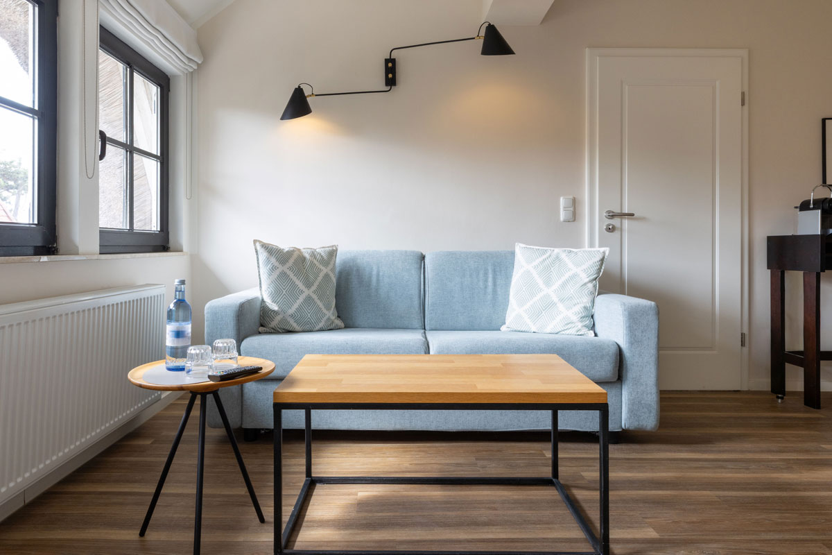 Wohnzimmer im Familienzimmer des STRANDHAUS Ahrenshoop mit blauem Sofa, Couchtisch und schwarzen Wandlampen.