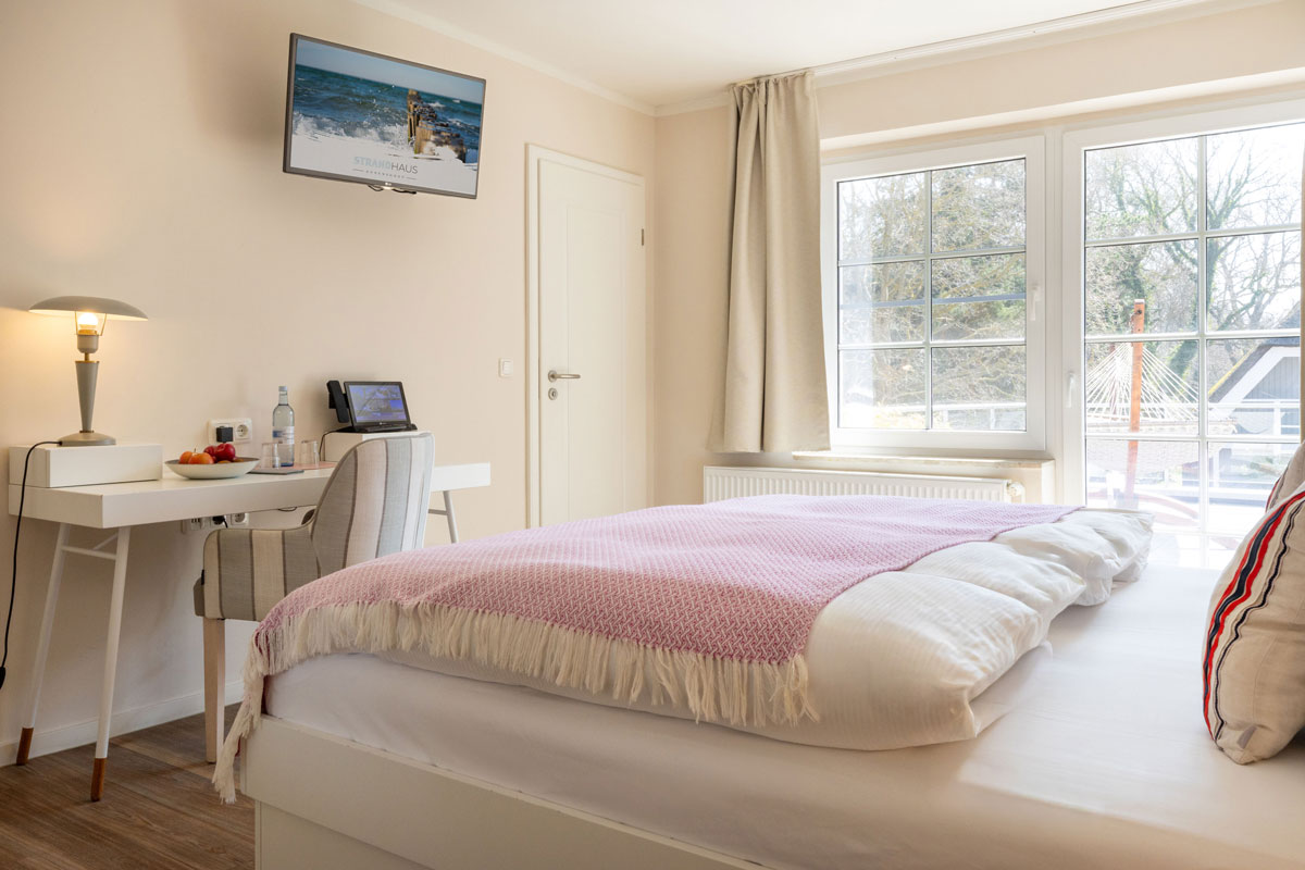 Doppelzimmer Sonnendeck im STRANDHAUS Ahrenshoop mit Doppelbett, Schreibtisch und Terrassentür zur Hängematte.