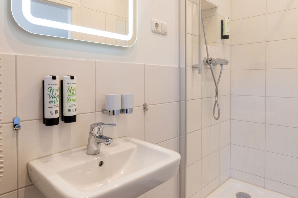 Helles Badezimmer der Terrassensuite im STRANDHAUS Ahrenshoop mit Waschbecken, Dusche und beleuchtetem Spiegel.