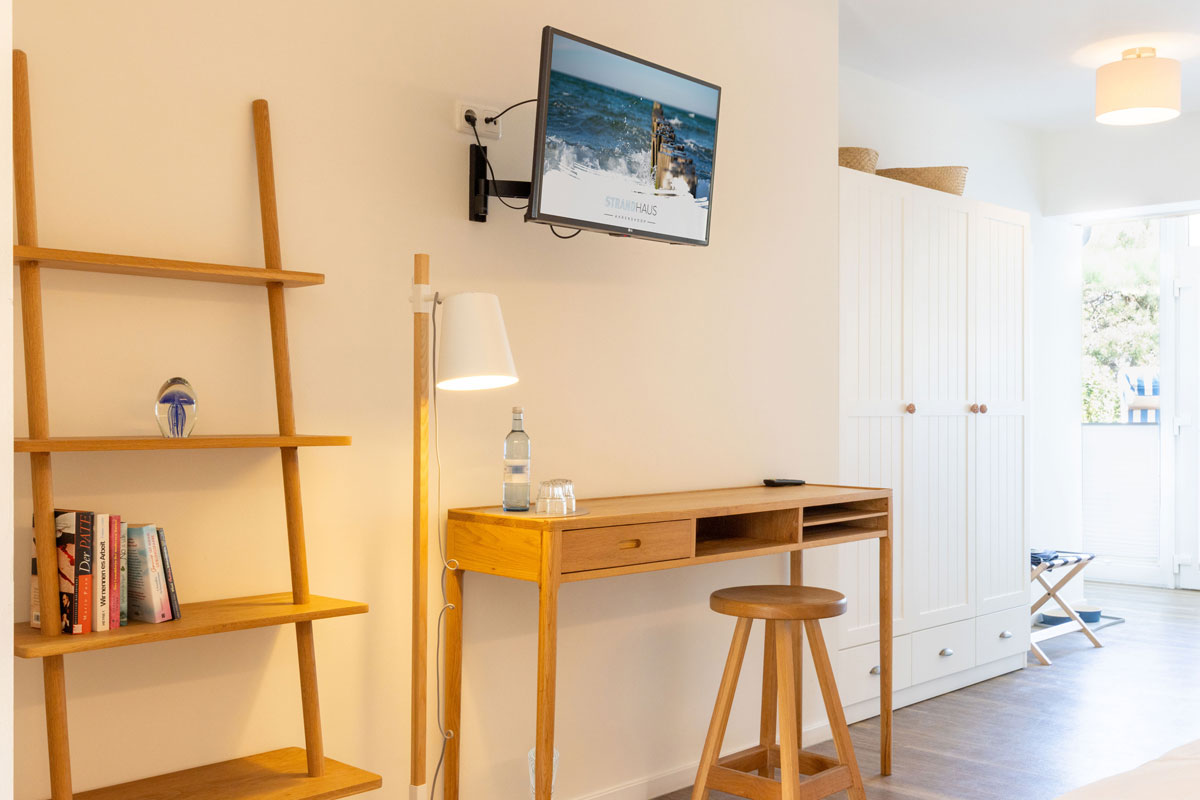 Wohnbereich der Terrassensuite im STRANDHAUS Ahrenshoop mit Holzschreibtisch, Leiterregal, Büchern und Wandfernseher.
