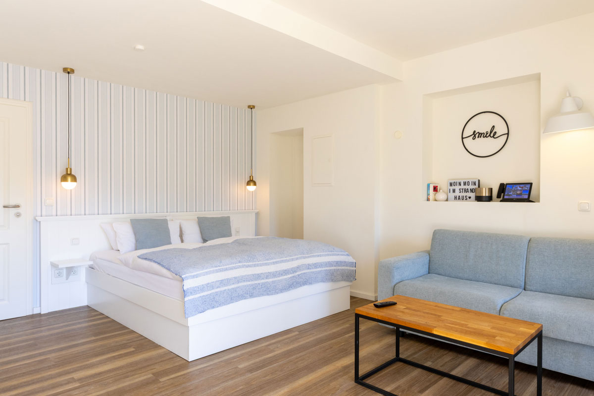 Terrassenzimmer im STRANDHAUS Ahrenshoop mit Doppelbett, blauem Sofa, Couchtisch und goldenen Pendelleuchten.