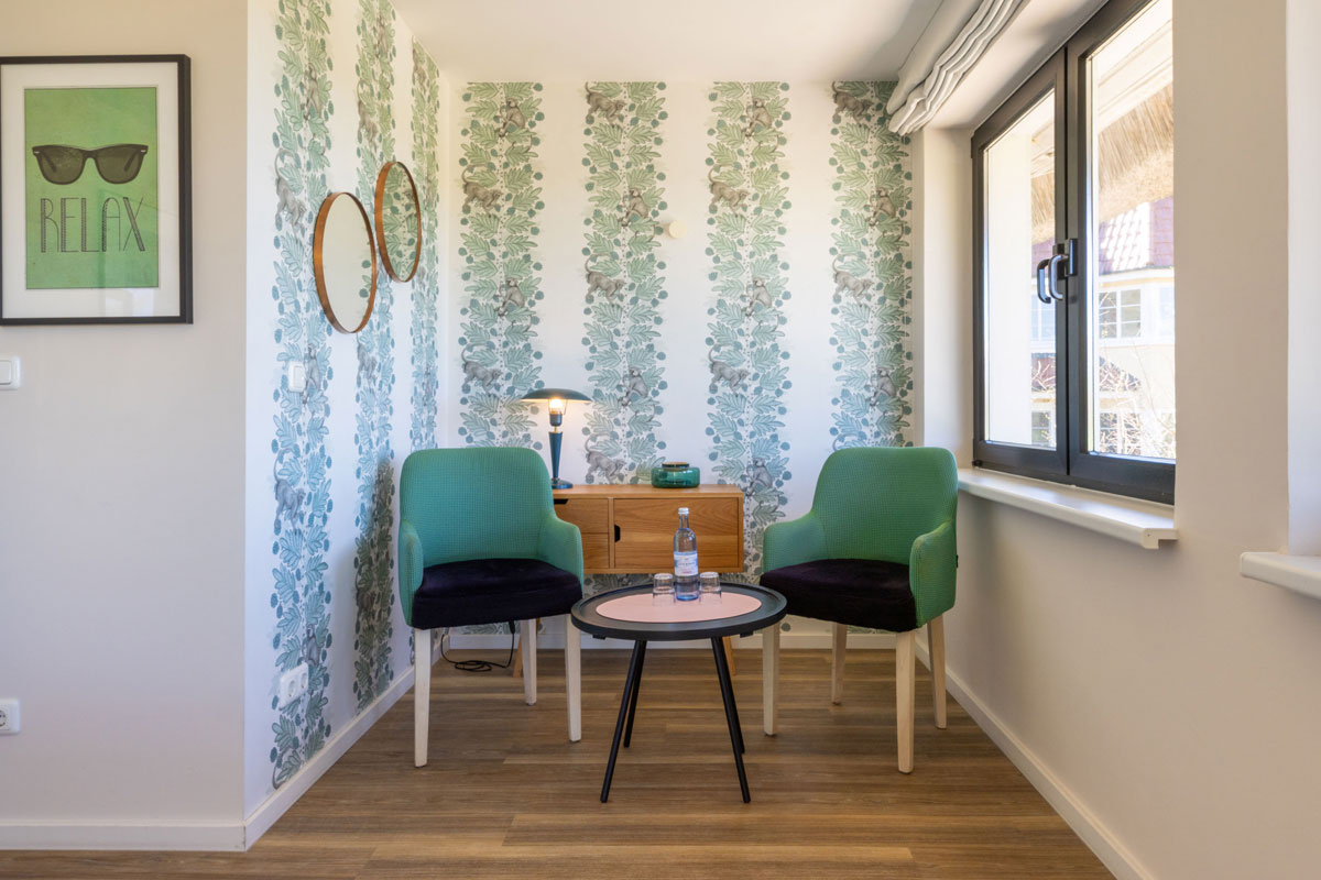 Sitzecke im Terrassenzimmer des STRANDHAUS Ahrenshoop mit zwei grünen Sesseln, rundem Tisch und floraler Tapete.